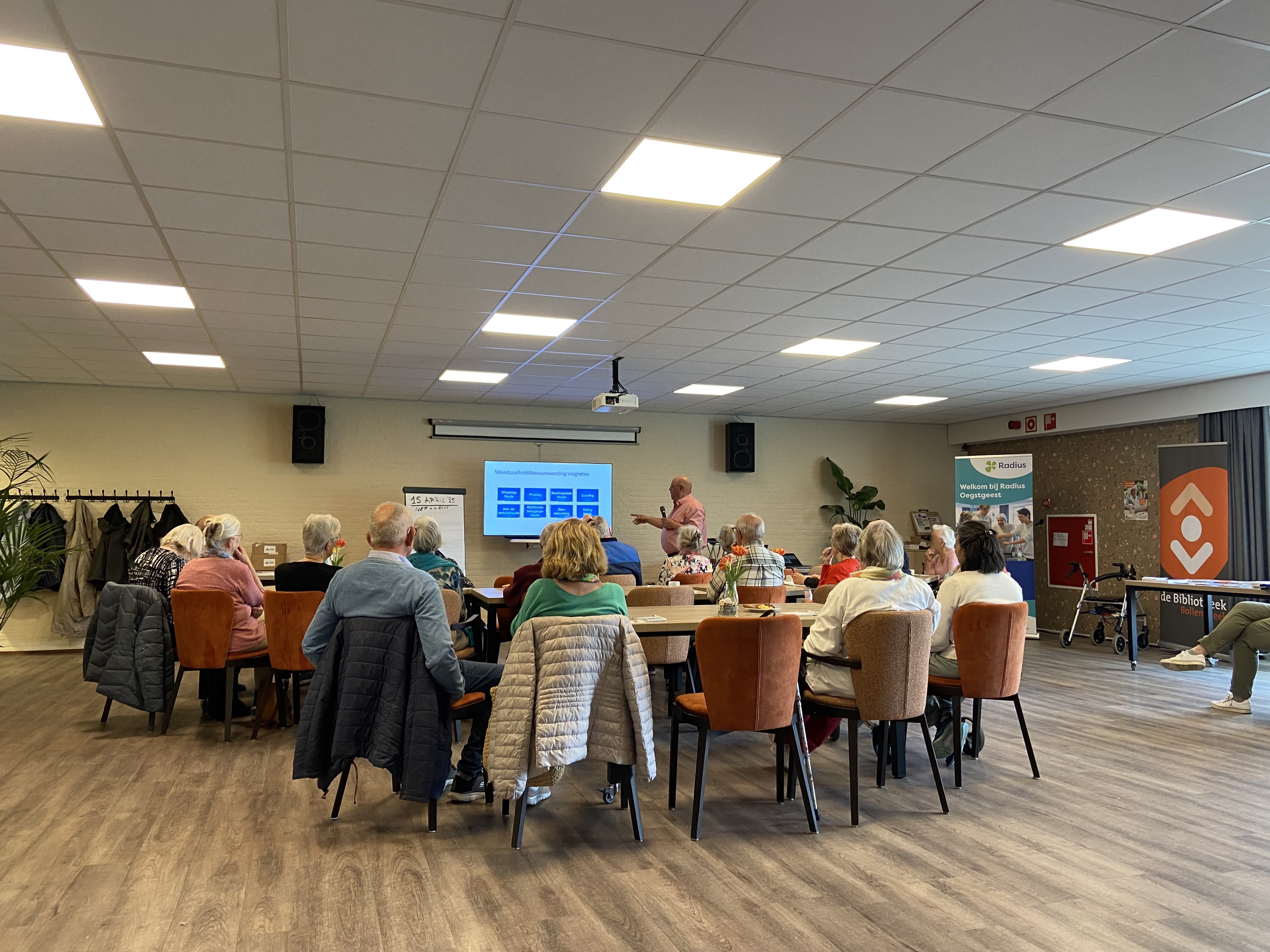 Een groep senioren volgt een presentatie op een groot scherm