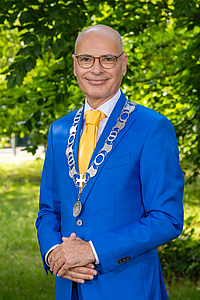 E.R. Jaensch (Emile), burgemeester met ambtsketen om in blauw pak met groen op achgergrond.