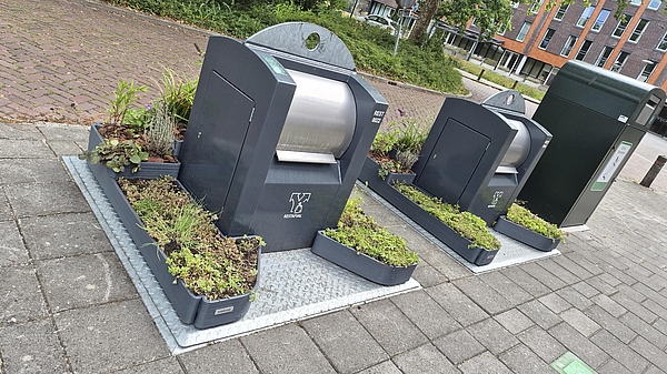 ondergrondse afvalcontainer met grijze plantenbakken eromheen geplant met verschillende groene plantjes